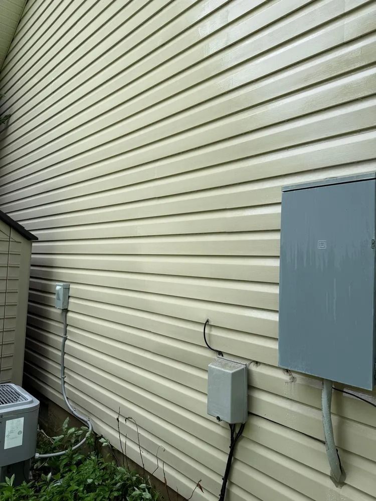 Light beige vinyl siding on a house wall with an electrical box, a disconnect switch, and a small utility meter.