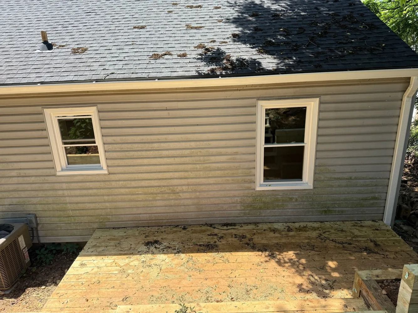 A beige-sided exterior wall of a house with two windows and a newly installed wooden deck beneath it.