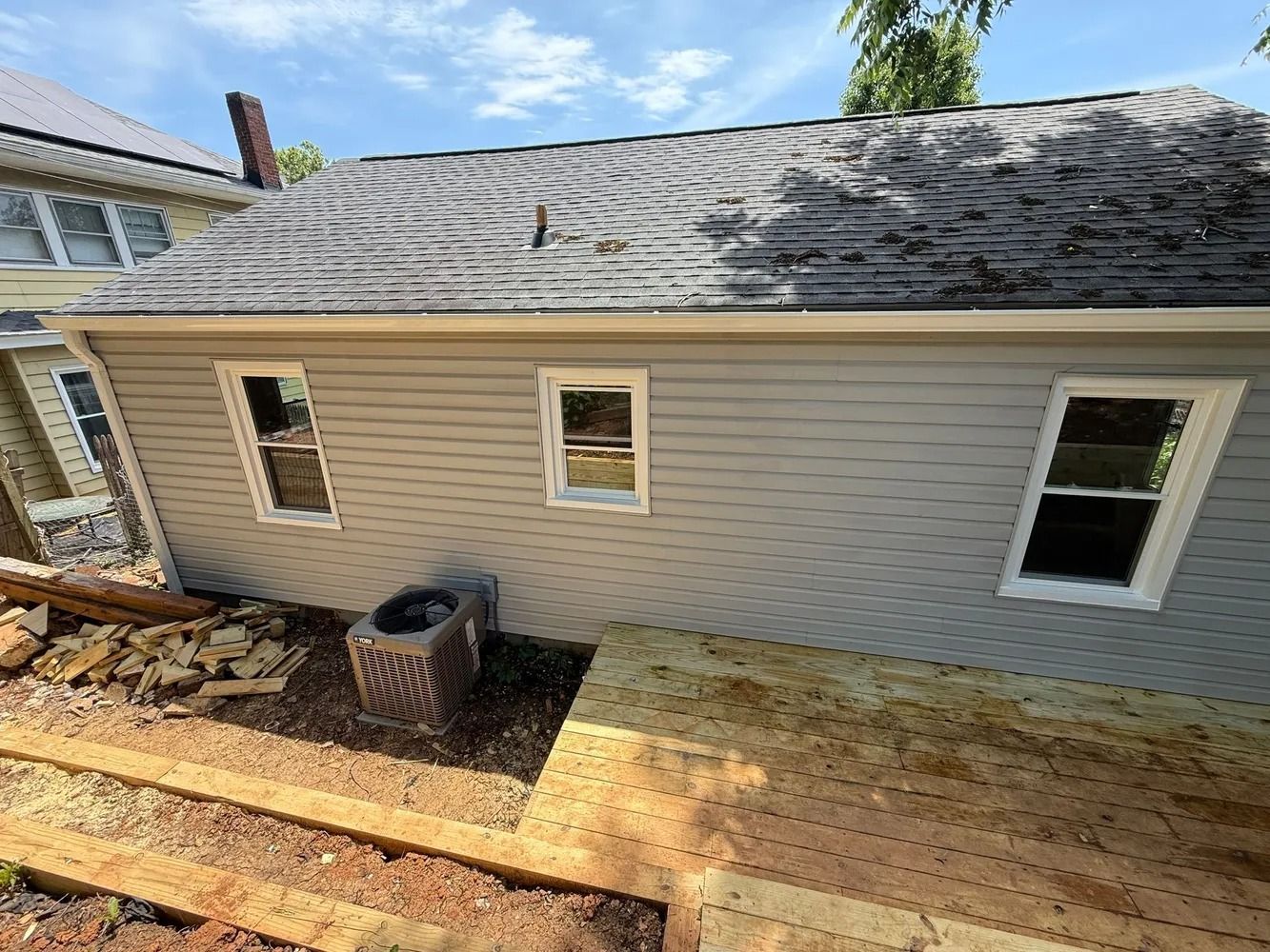 A gray-sided house exterior with three windows, a roof, and an adjacent wooden deck under construction.