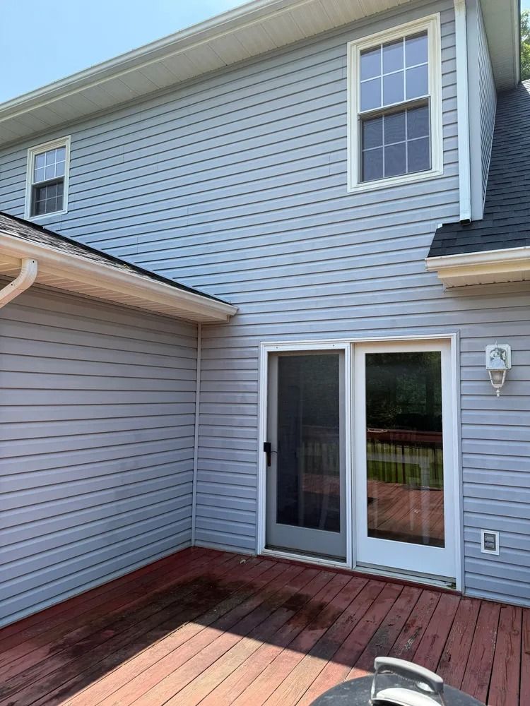 A light blue house exterior featuring a wooden deck, a sliding glass door, and two windows.