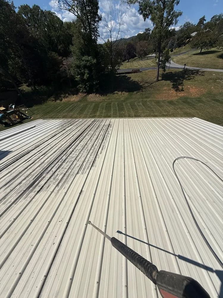 Pressure washing a large, corrugated metal roof, showing a clean path being created across the dirty surface.