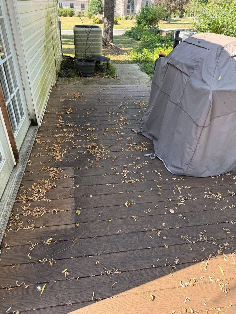 A wooden deck covered in scattered leaves, with a covered grill on the right and a house wall on the left.