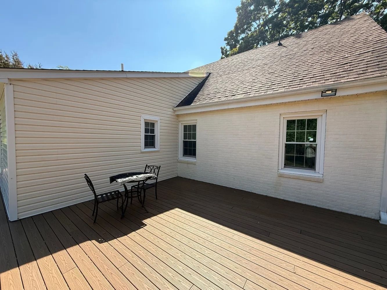 A beige-sided house with a wooden deck and a small bistro table and chairs sitting in the corner.