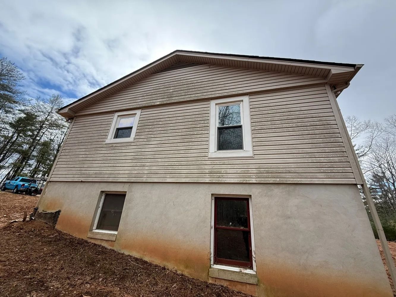 The side view of a two-story house with wavy light-colored vinyl siding above a foundation wall with two windows.