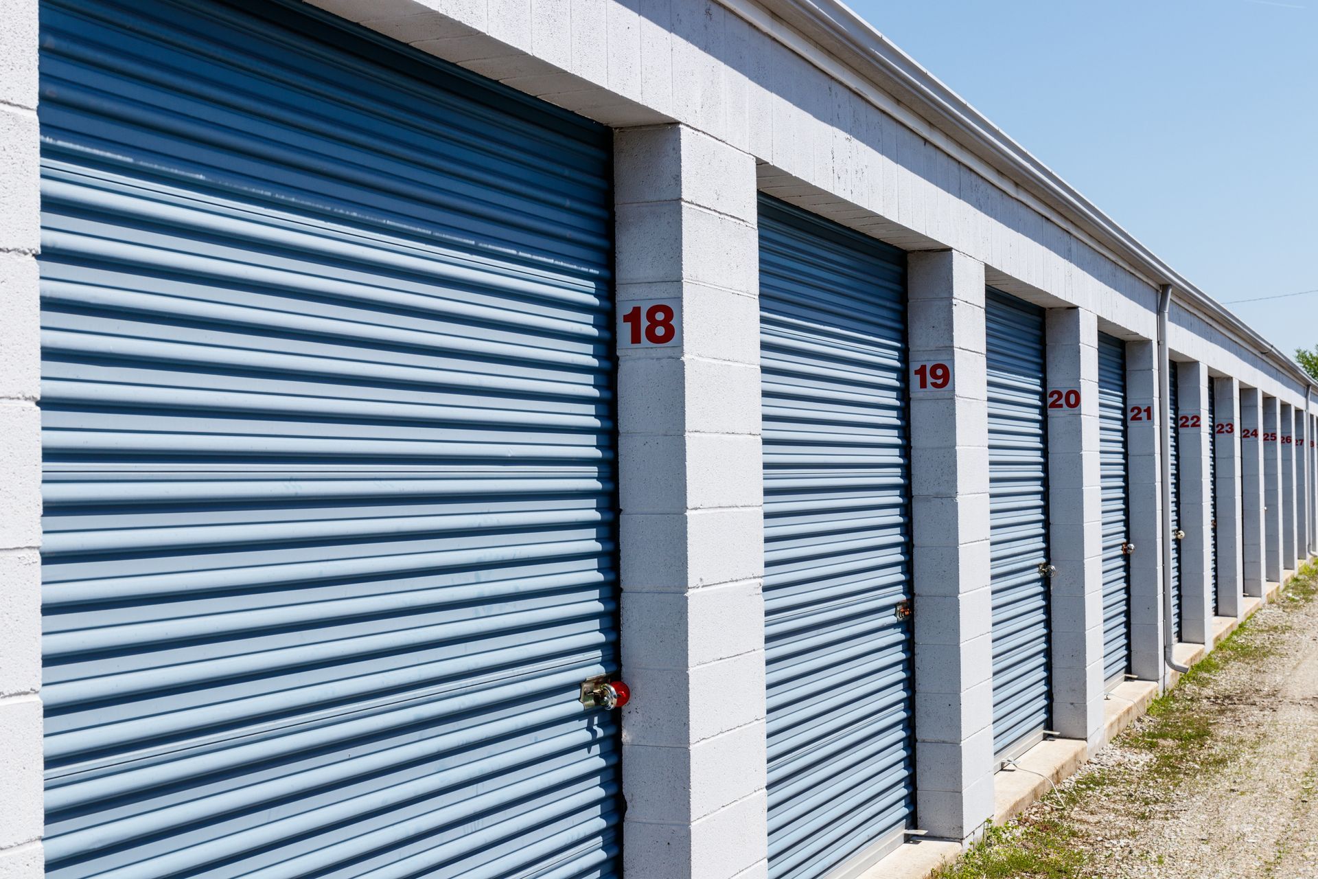 Storage units with blue metal doors, numbers 18-22 in red, along a cement structure.