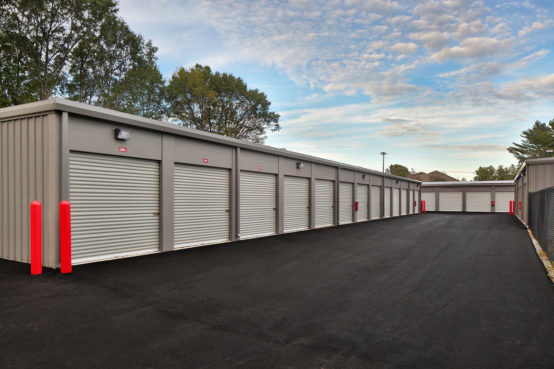 Exterior view of a self-storage facility with several grey units and a black asphalt driveway.
