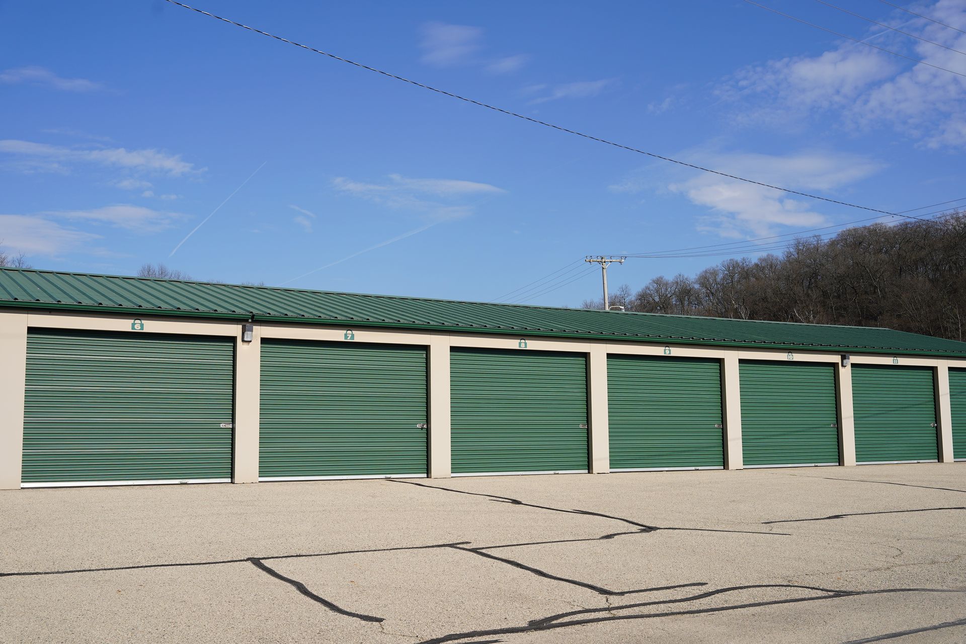 Storage units with green doors and roof under a blue sky.