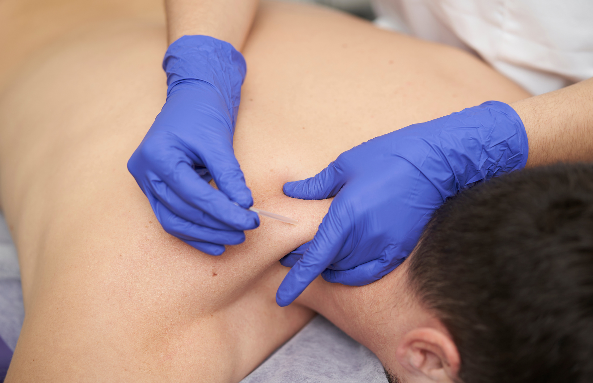 Gloved hands performing a back massage on a person lying face down