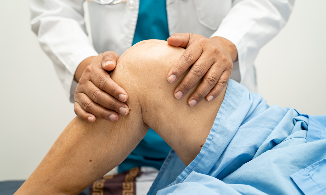Doctor examining a patient's knee, hands on the knee, in a medical setting.