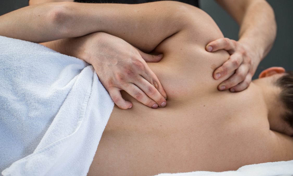 Person receiving back massage. Therapist's hands on shoulder, covered by white towel, indoors.