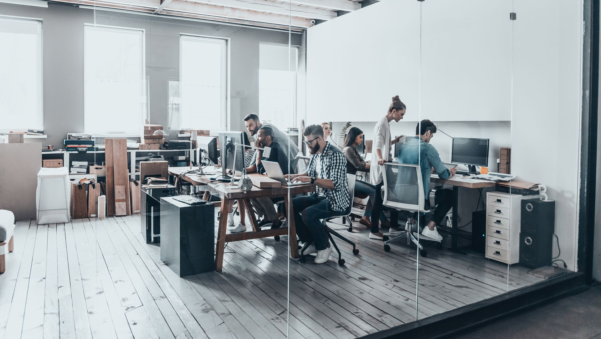 Modern office with people working at desks, enclosed by glass walls.