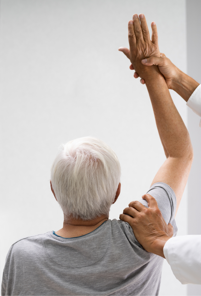 Doctor assisting elderly patient with arm movement in a white room.