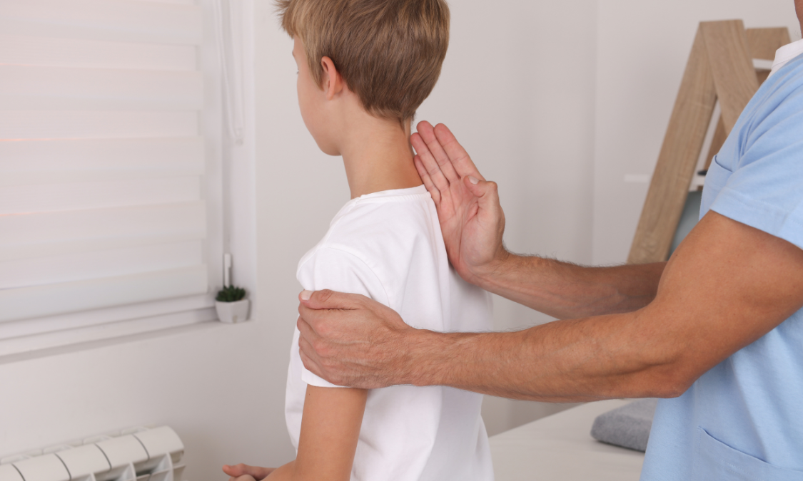 Doctor examining a young boy's posture. White shirts, light-skinned people in a medical office.