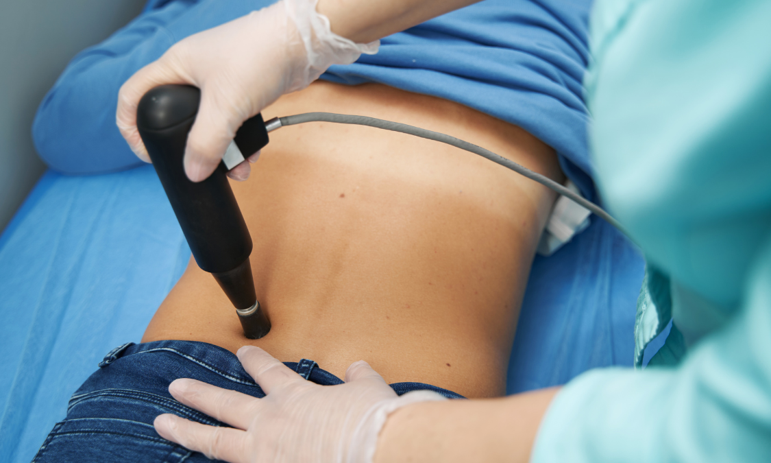 Person receiving back therapy with a device held by a person in medical gloves.