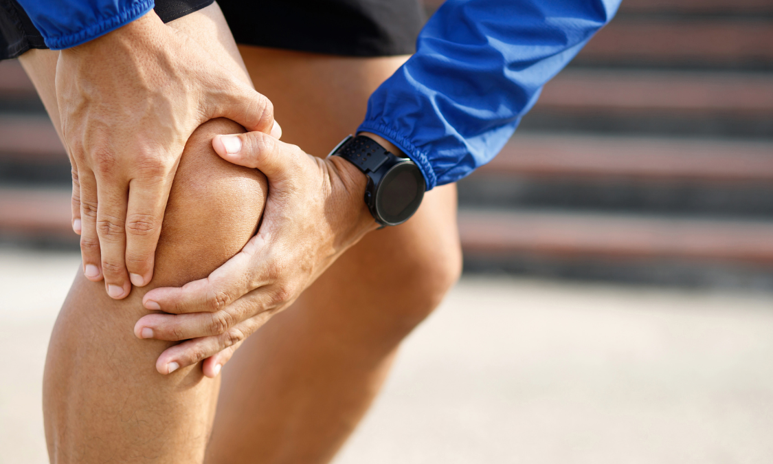 Man holding his knee in pain, possibly injured during exercise outdoors.