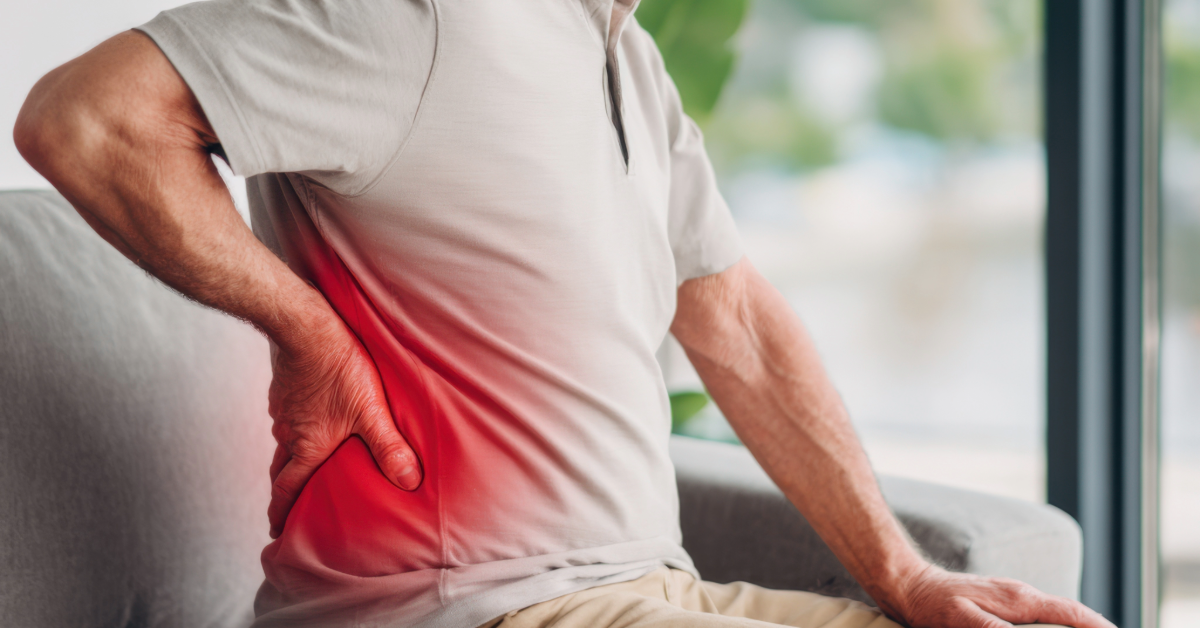 Man sitting, holding lower back, indicated in red for pain.