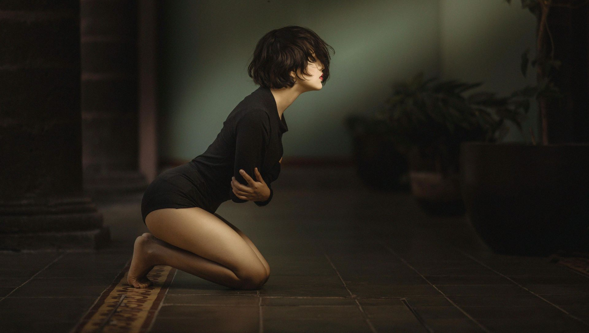 Woman kneeling, hugging herself, in a dark room.