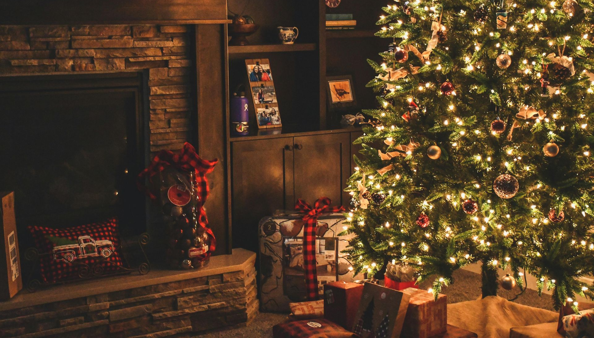Christmas tree with lights and ornaments beside a fireplace, gifts, and stockings.