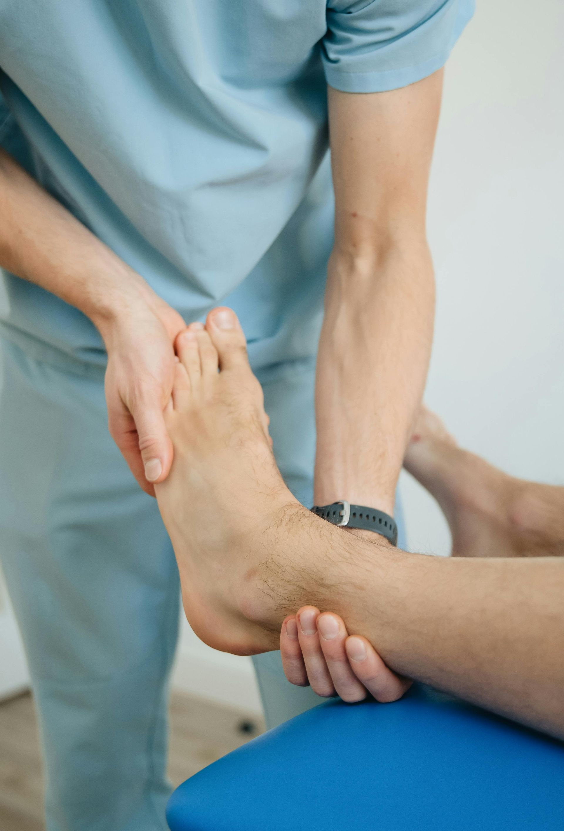 Person in blue scrubs examining a foot on a blue surface.