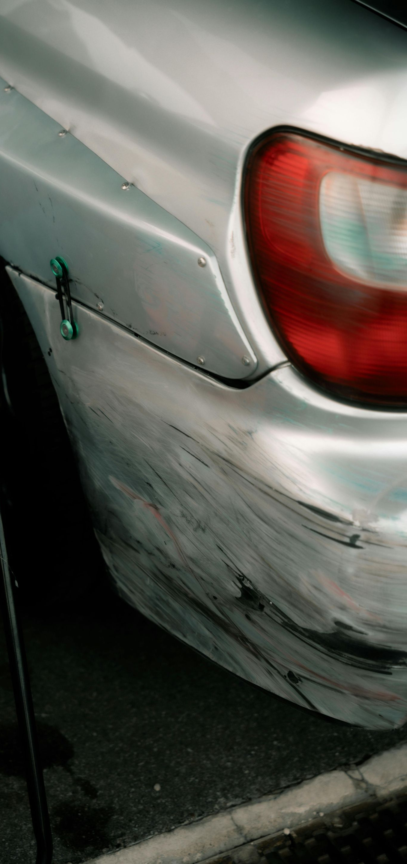 Silver car with significant damage to the rear bumper, next to a black chair with a pink seat.