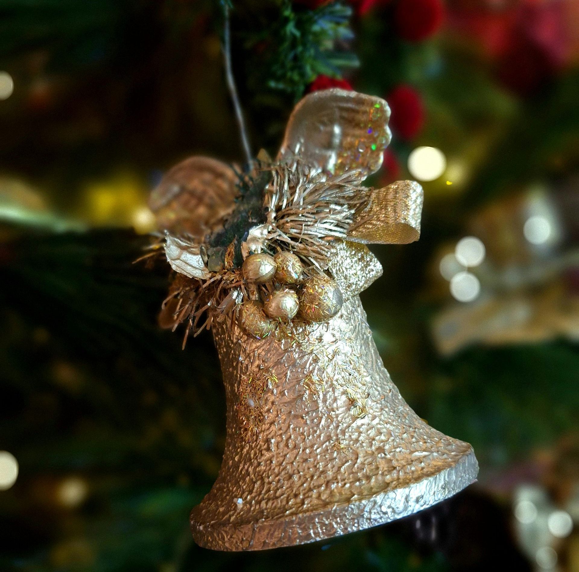Gold glitter bell Christmas ornament on a tree.