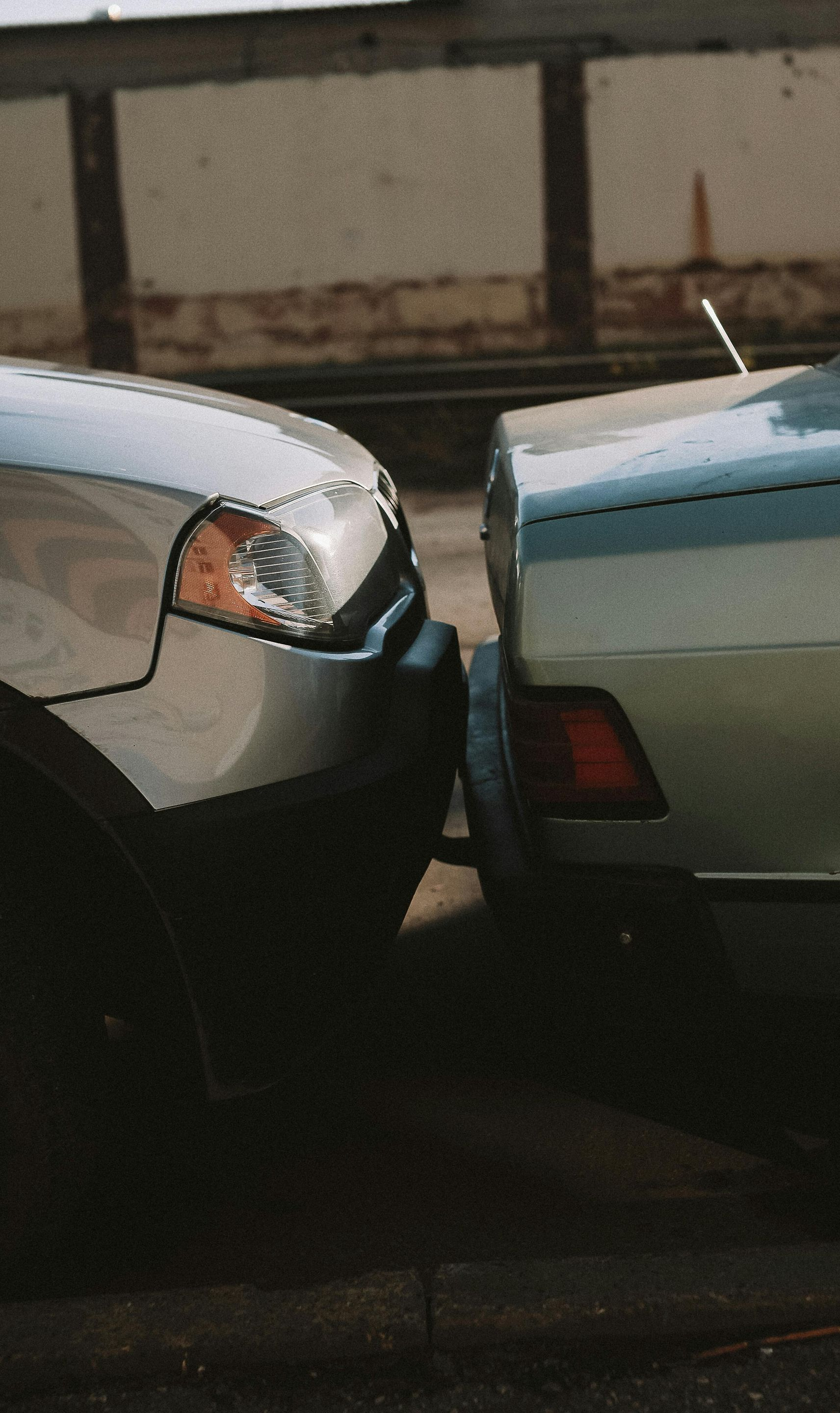 Two cars, silver and blue, bumper-to-bumper in an outdoor setting.
