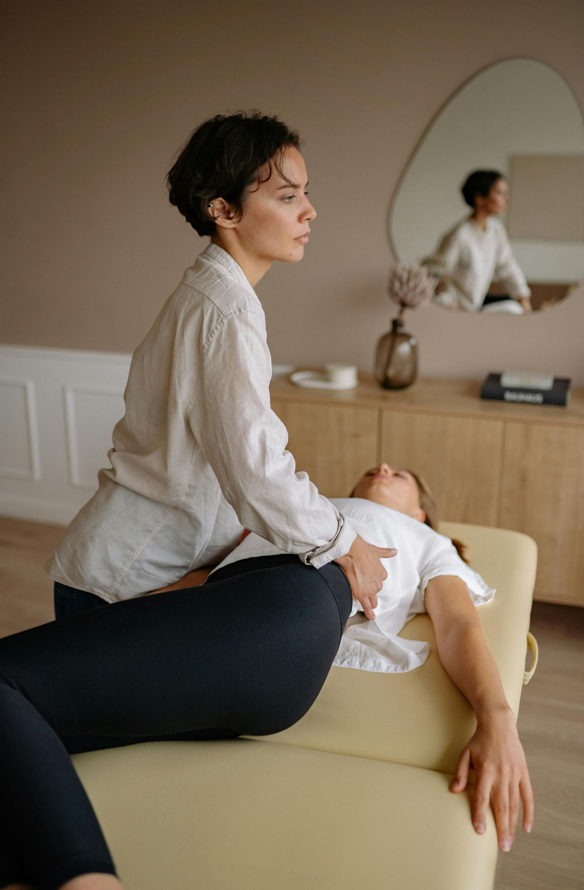 Woman giving massage to another woman lying on a massage table. Indoor setting.