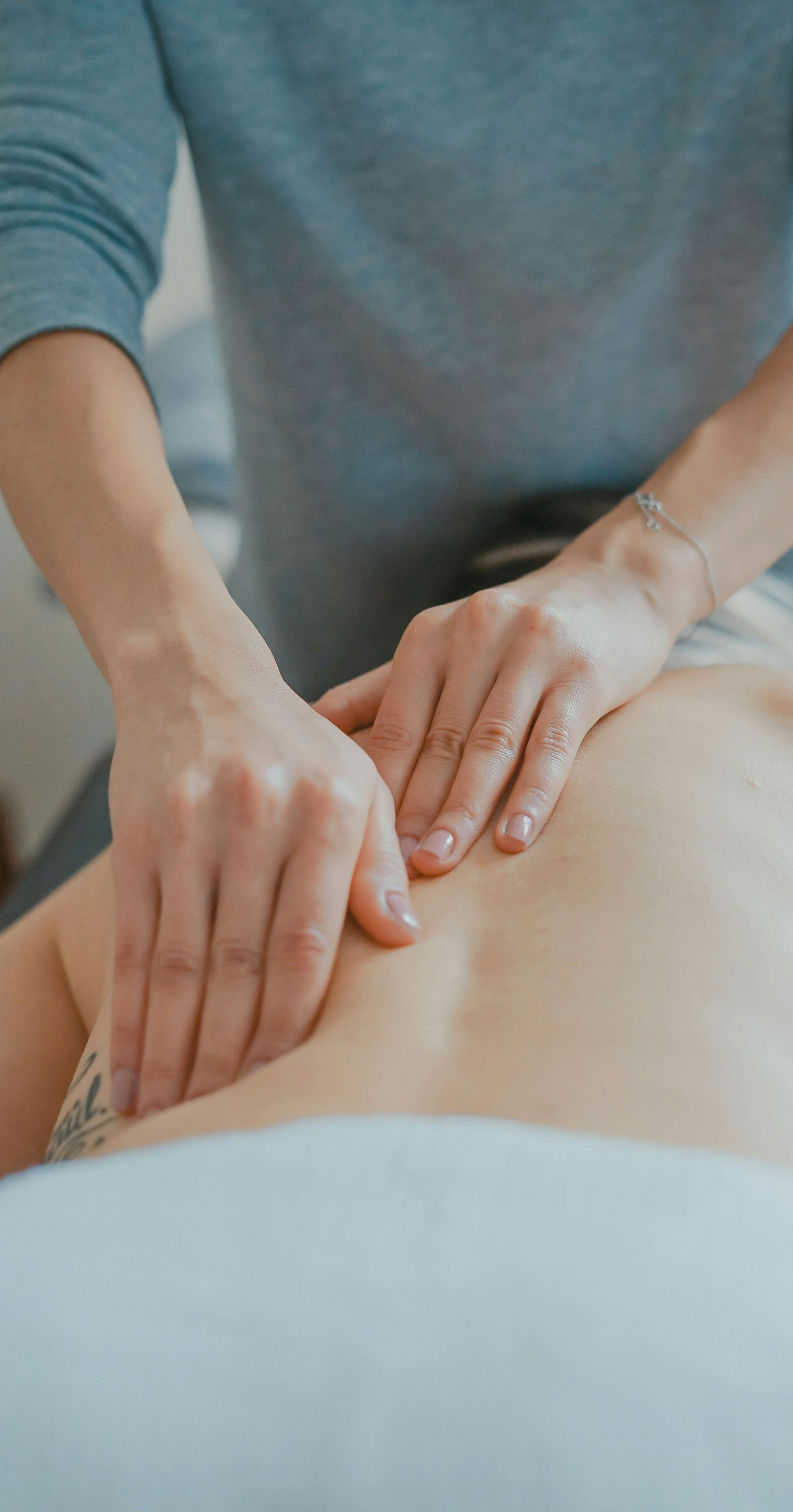 Hands massaging a person's back; light blue shirt; white sheets.