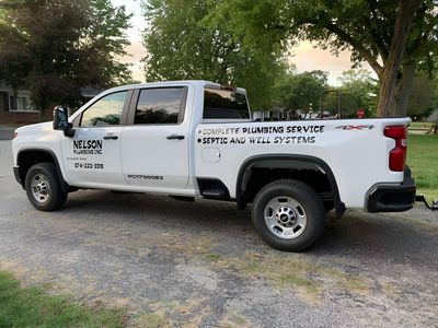 White landscaping service pickup truck parked on a gravel driveway beside trees and a house