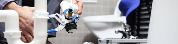 Plumber repairing a sink pipe with tools in a kitchen sink area