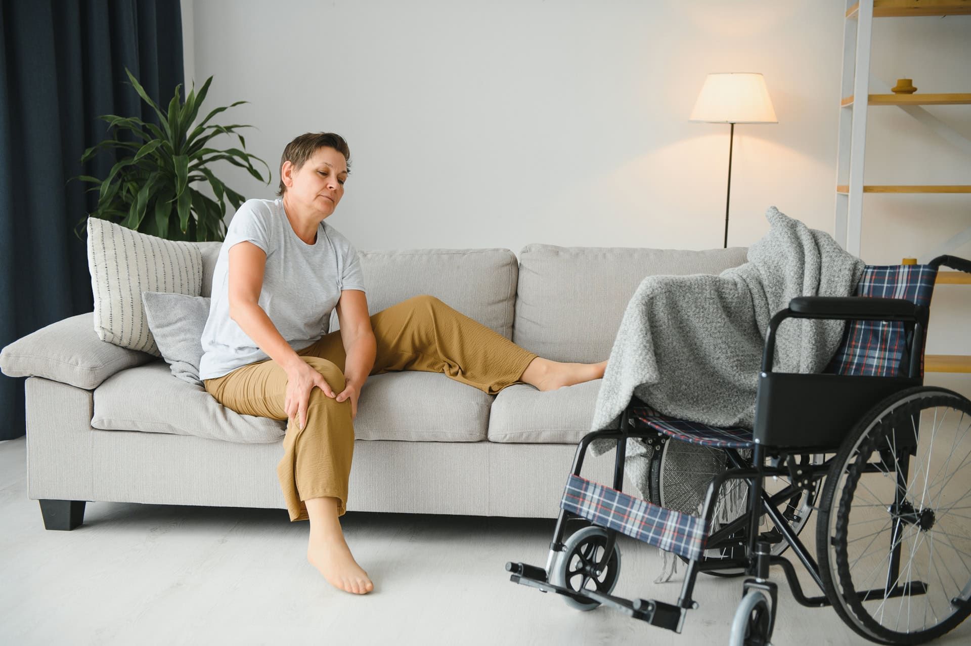 A woman is sitting on a couch next to a wheelchair.