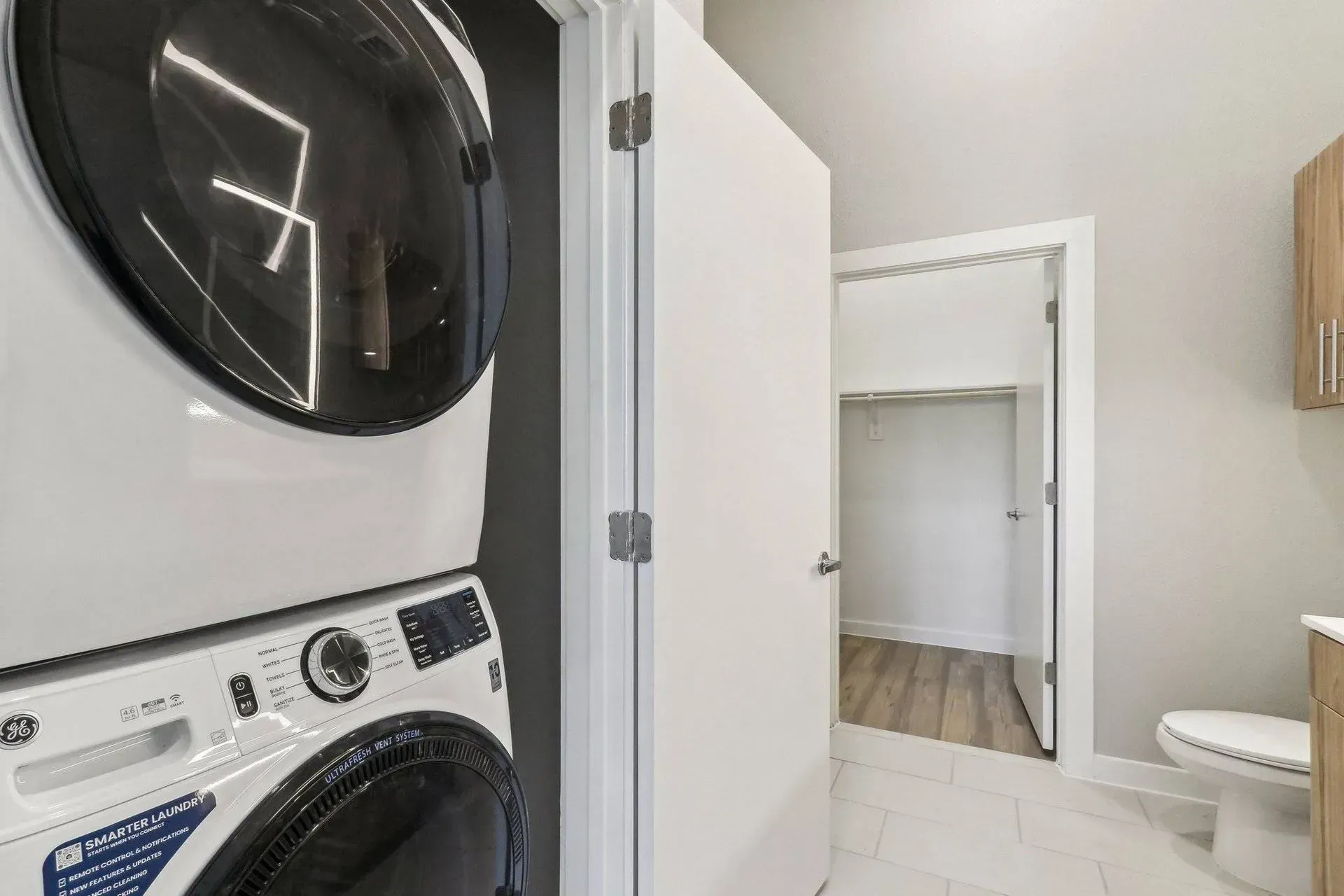 Stacked GE washer and dryer in a laundry room with a white door and closet.