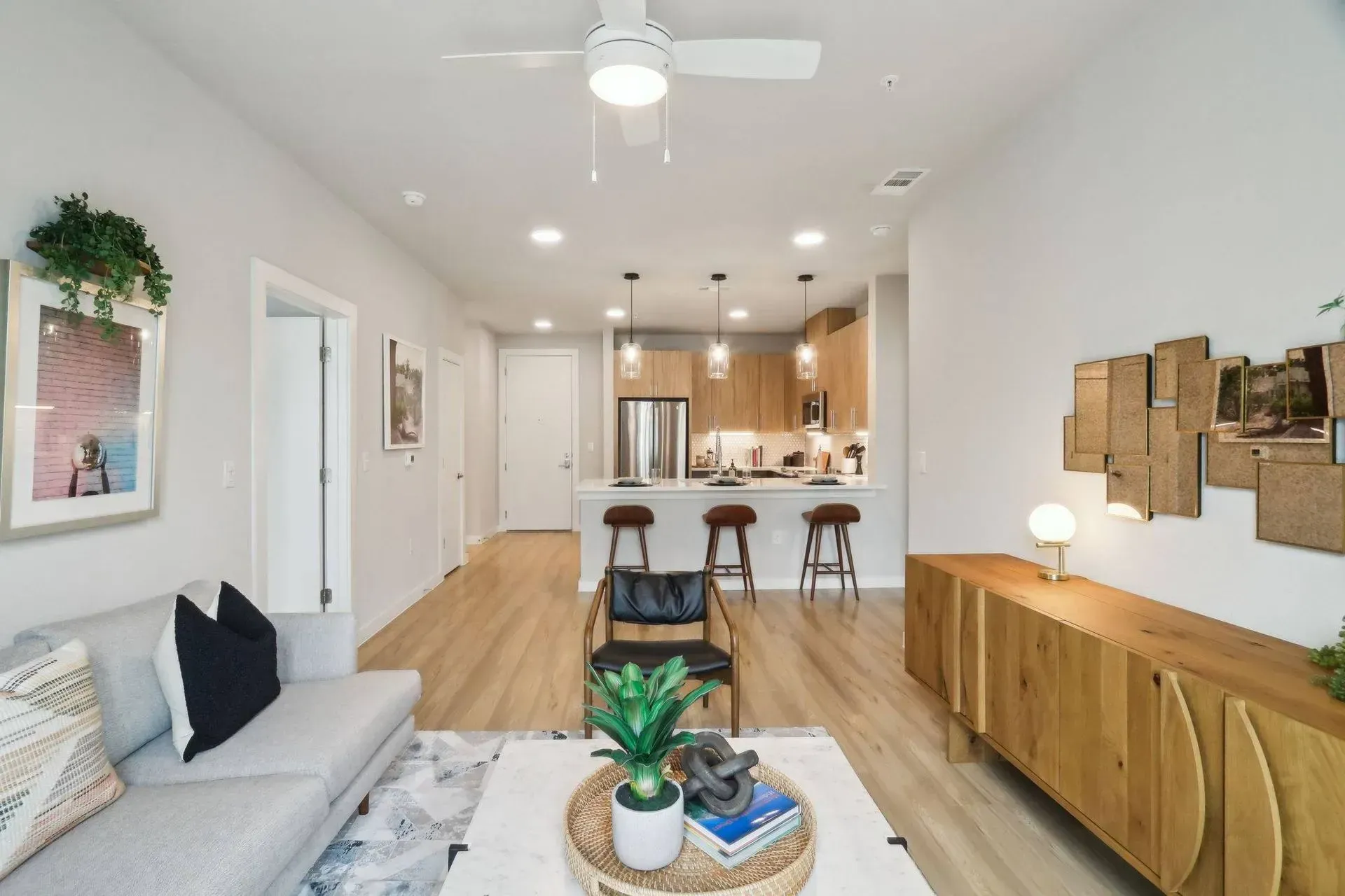 Modern open-plan apartment interior with living room, kitchen, light wood floors, and neutral tones.