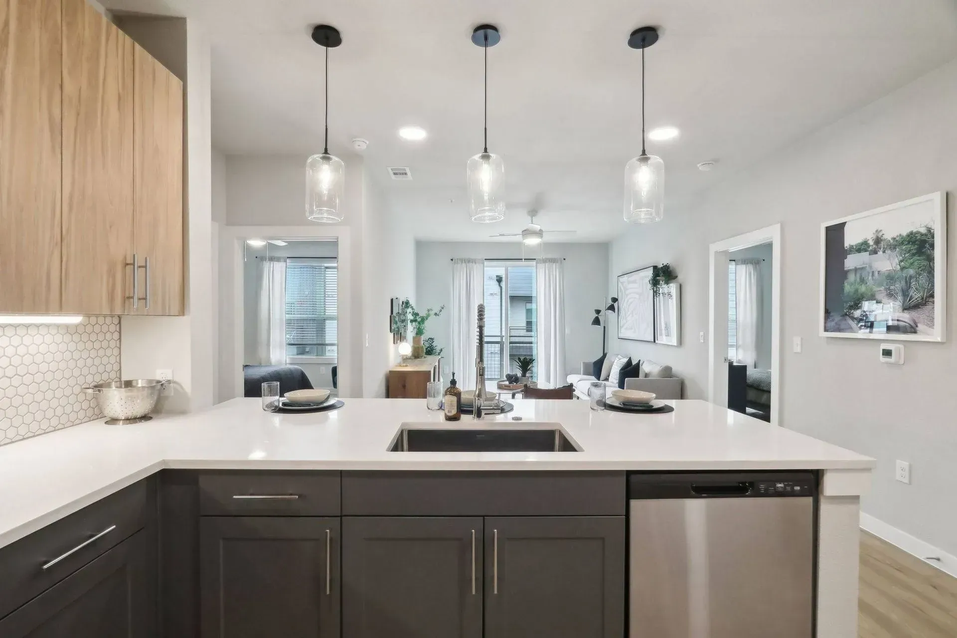 Modern kitchen with island, pendant lights, and stainless steel appliances. View into living area.