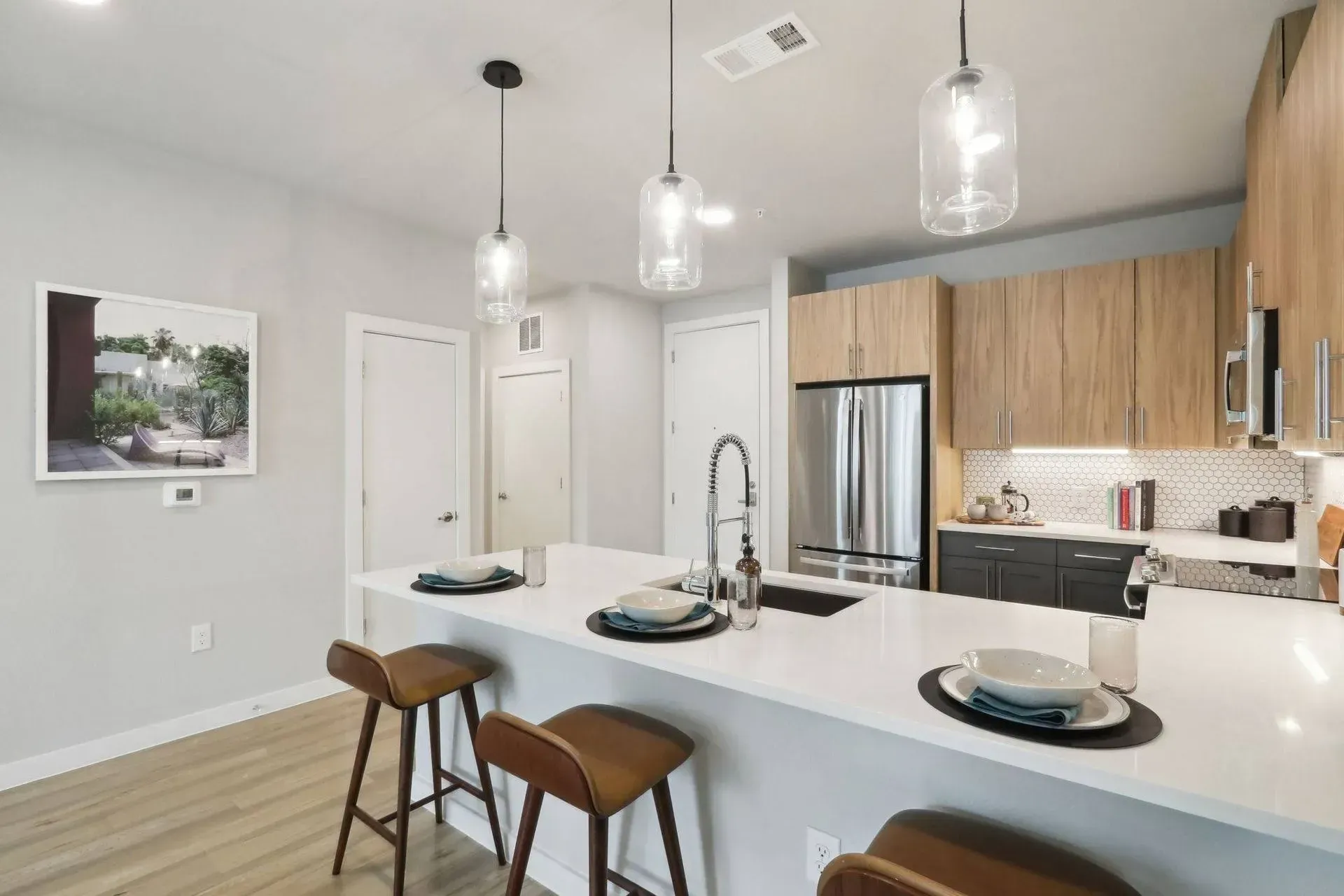 Modern kitchen with light wood cabinets, white island, and three pendant lights.