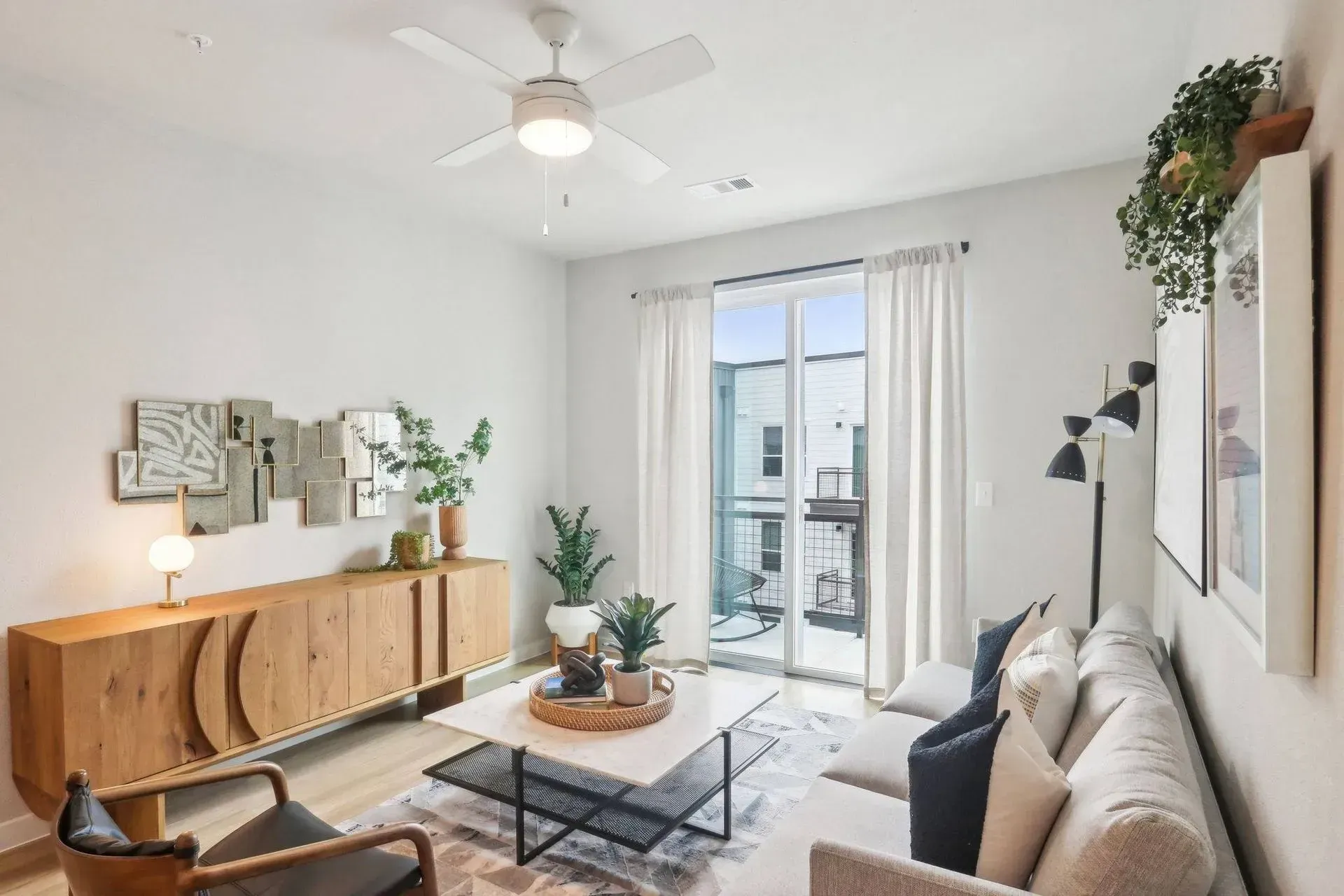 Modern living room with light wood cabinet, white sofa, plants, and balcony.