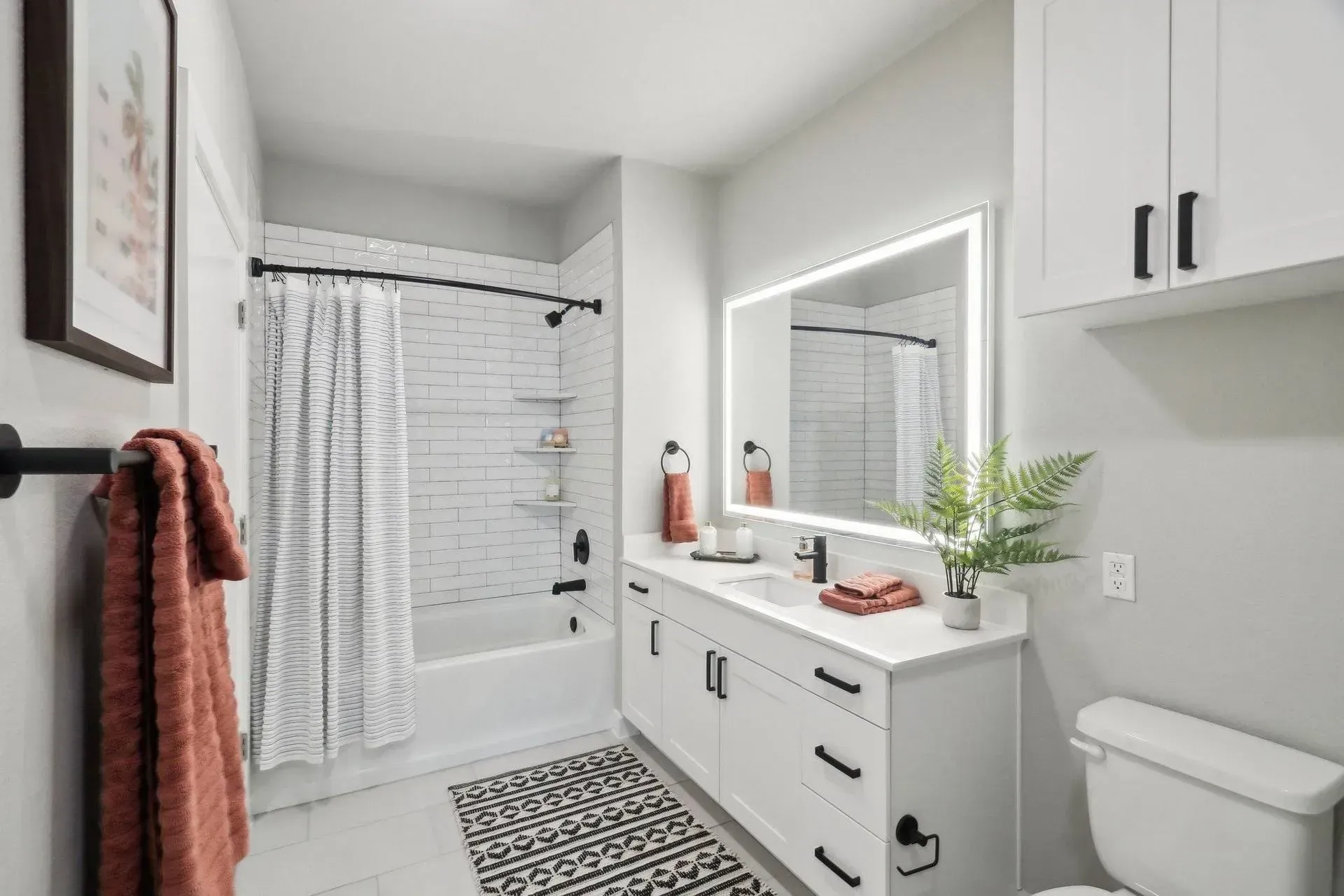 White modern bathroom with a tub, white vanity, and black accents.