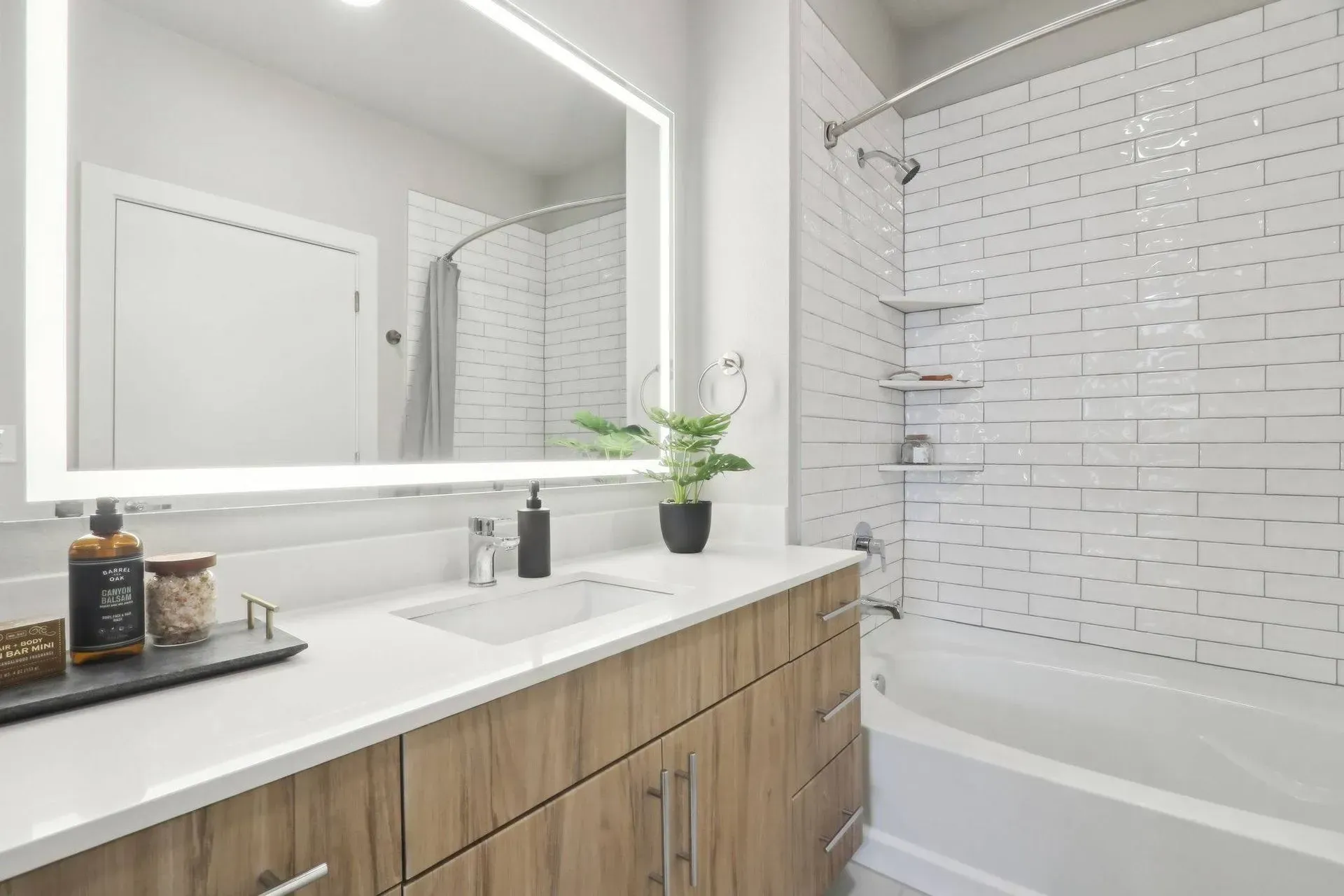 Bathroom with wood vanity, white countertop, large mirror, and white tiled shower.