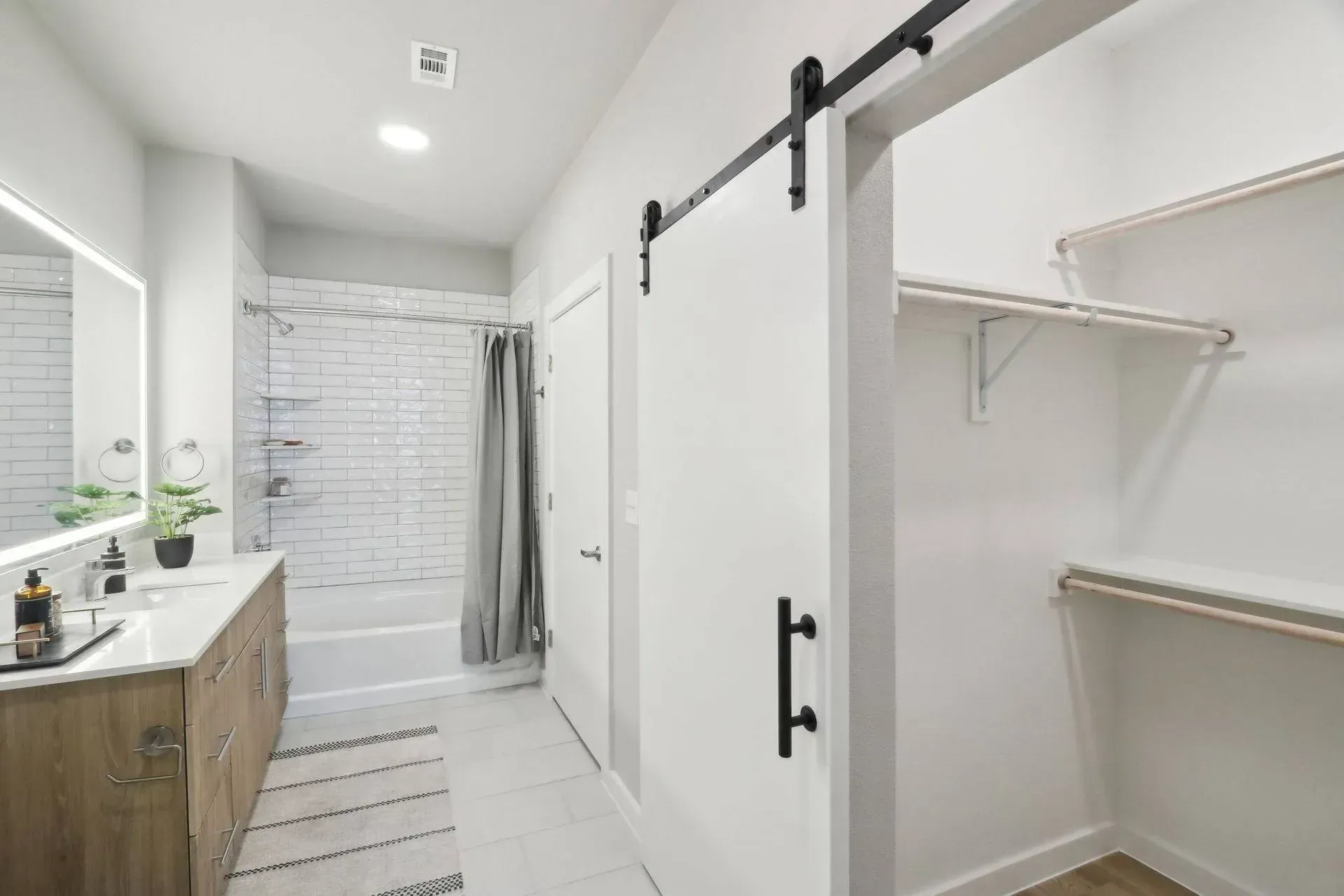 Bathroom with a white barn door leading to a closet with shelves; a vanity with a mirror is on the left.