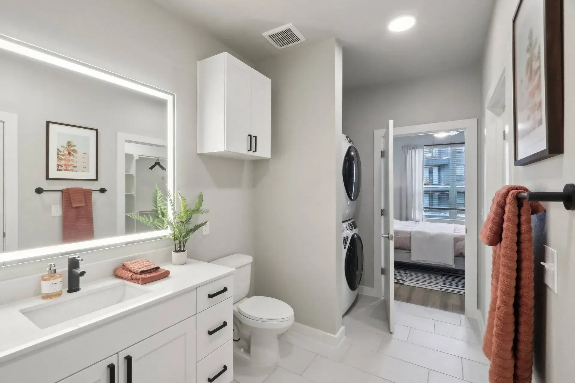 Bathroom with white cabinetry, stacked washer and dryer, and doorway to a bedroom.