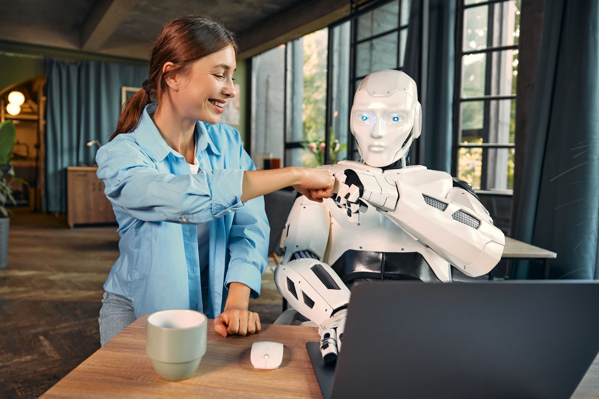 Een vrouw speelt met een robot achter een laptop.