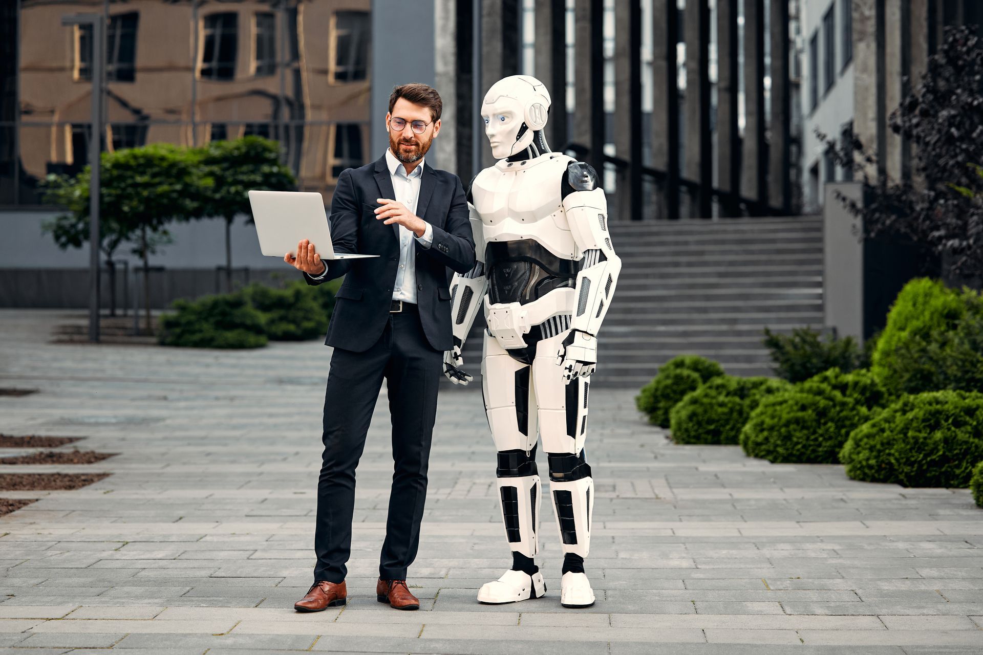 Een man in een pak staat naast een robot die een laptop vasthoudt.