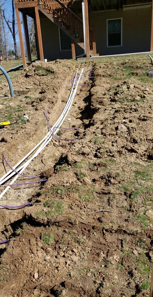 Trenched ground with white and purple pipes leading towards a building with a deck.