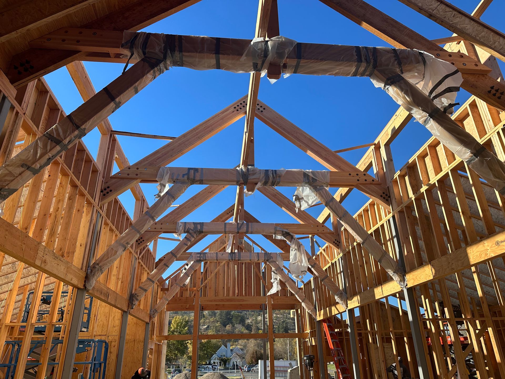 Wooden house frame with rafters, braces, and a clear blue sky.