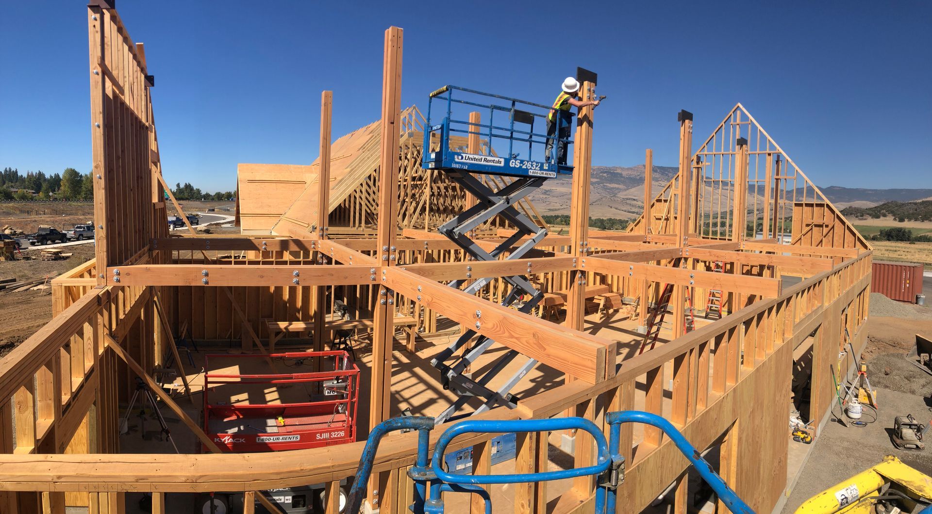 Construction workers on a lift framing a two-story wooden house under a blue sky.