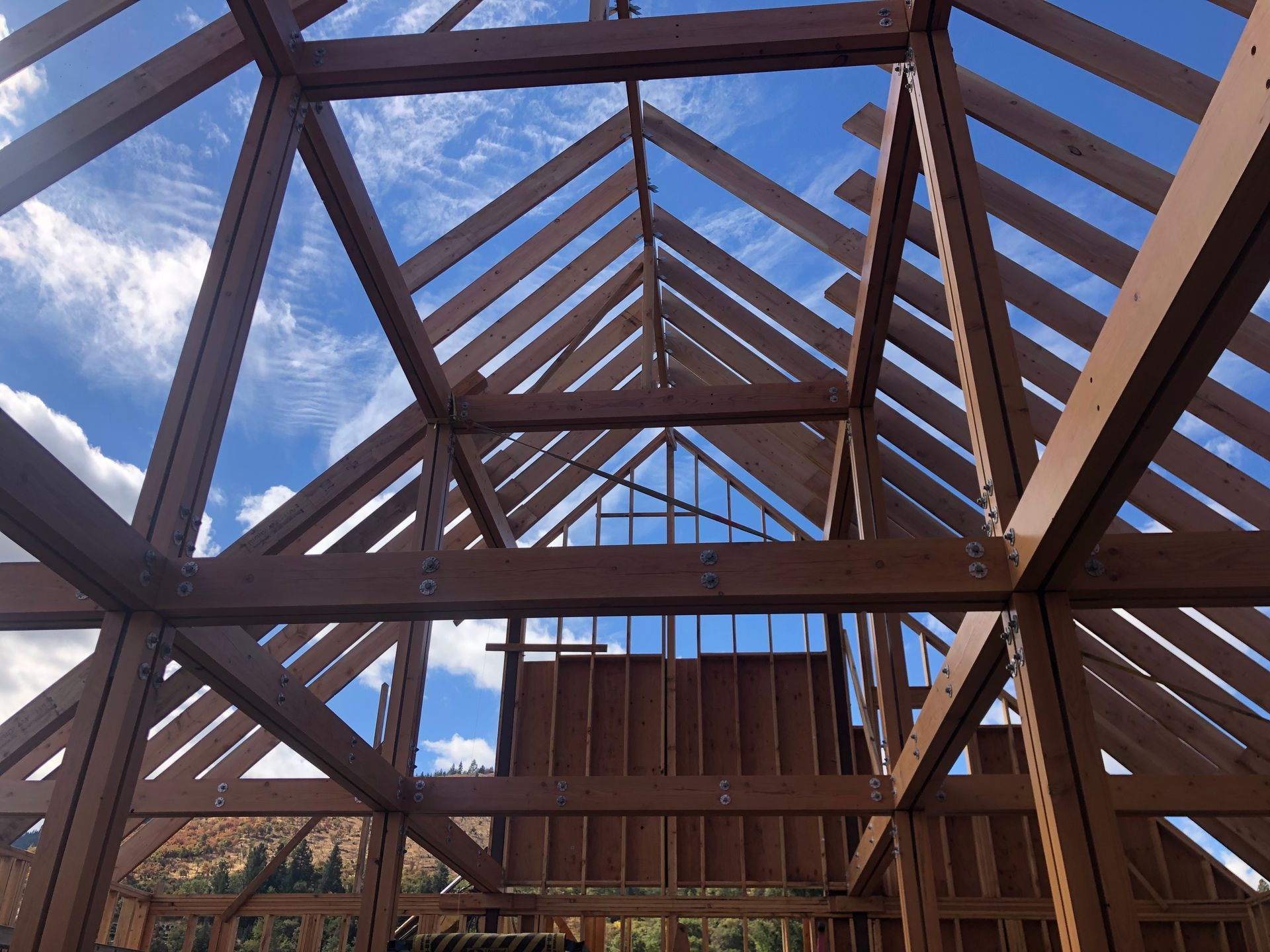 Wooden structure of a building under construction against a blue sky, showing beams and rafters.