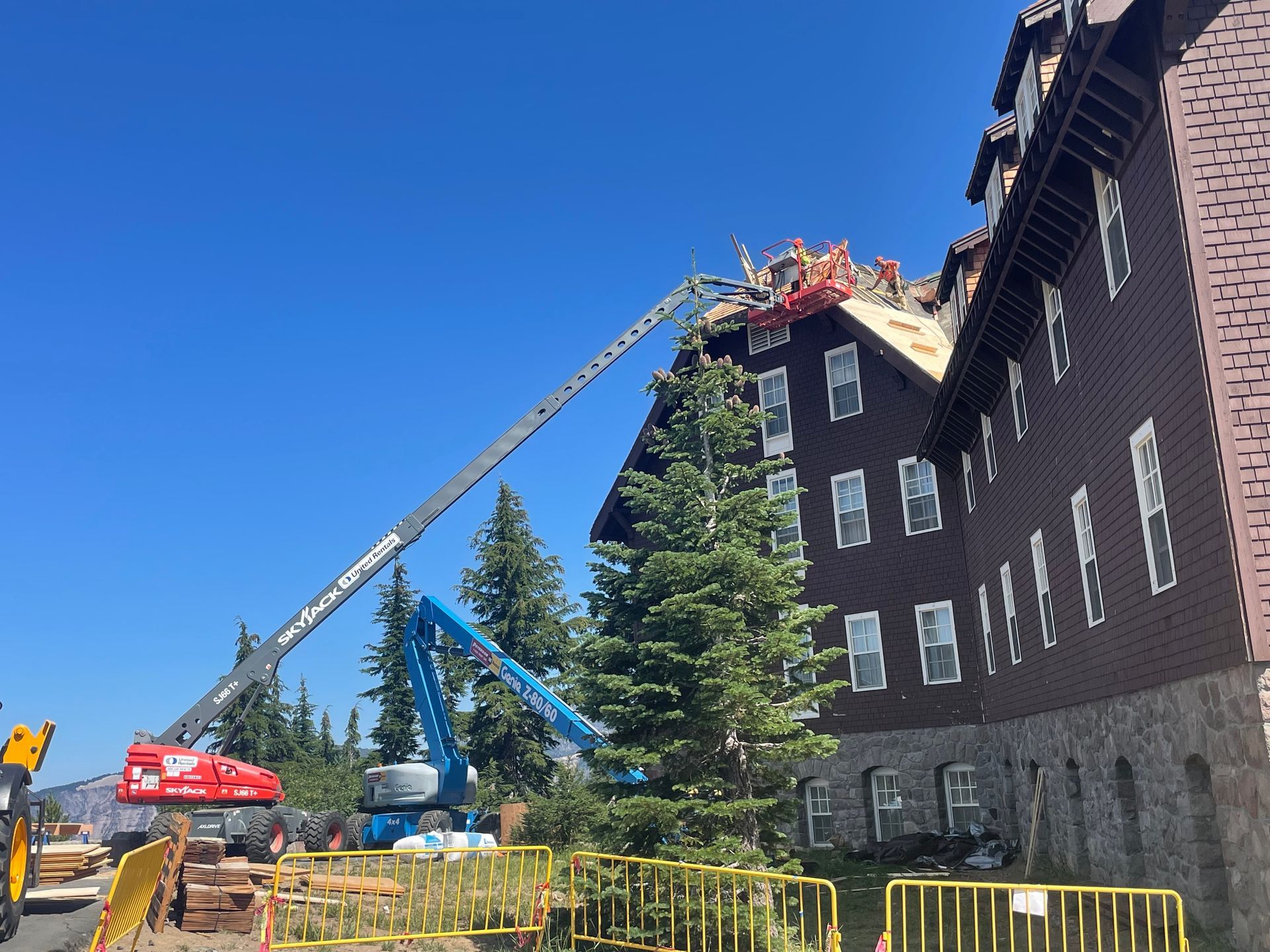 Construction crew on a building's roof using lifts. Blue sky overhead.