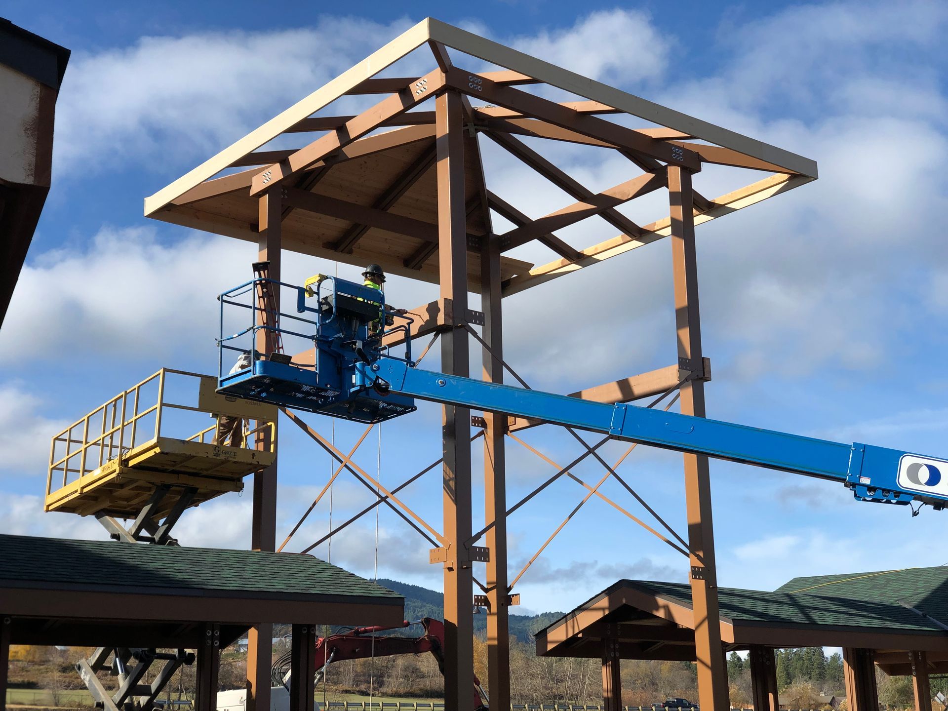Construction worker on a lift working on a brown wooden tower roof.