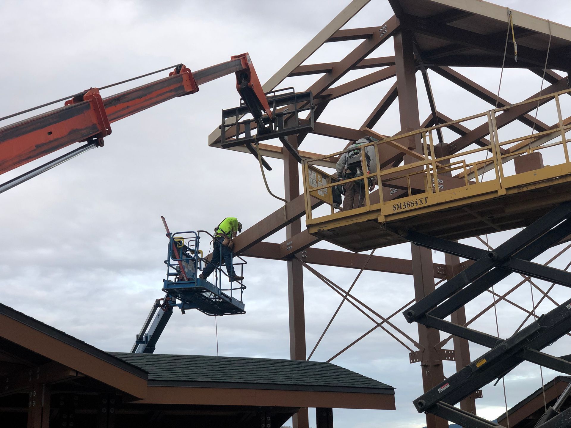 Construction workers on lifts assembling steel framework. Gray sky backdrop.