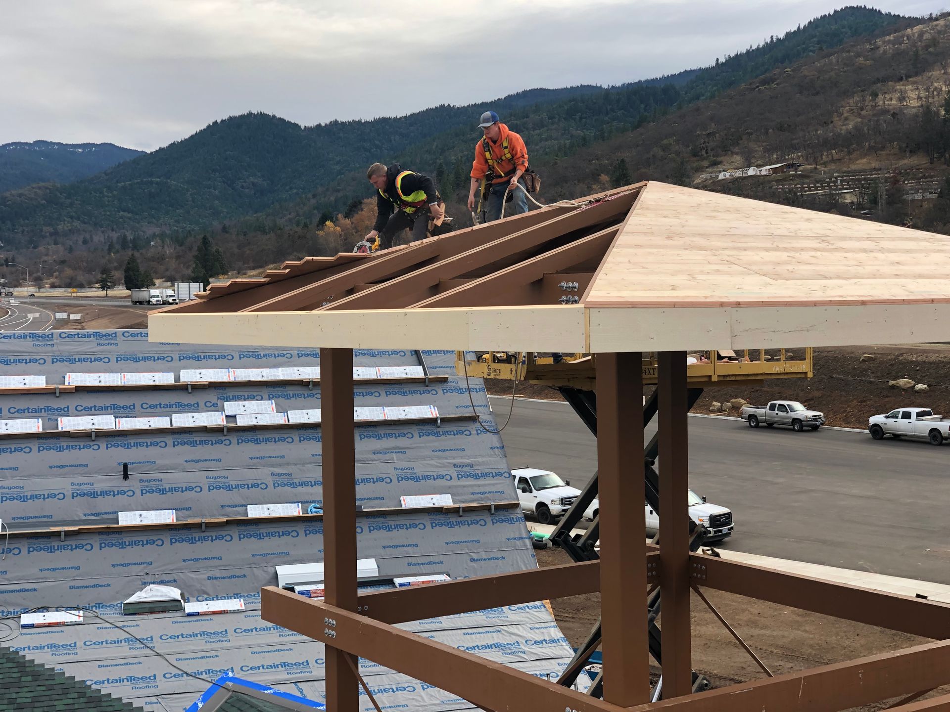 Construction workers on a roof, installing wooden beams. Mountains in the background.